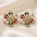 Gold-tone snowflake stud earrings with red and green stones, clear centres, and white pearl-like beads on ivory satin