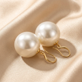 Round ivory-white pearl-look earrings with gold-tone fittings on satin
