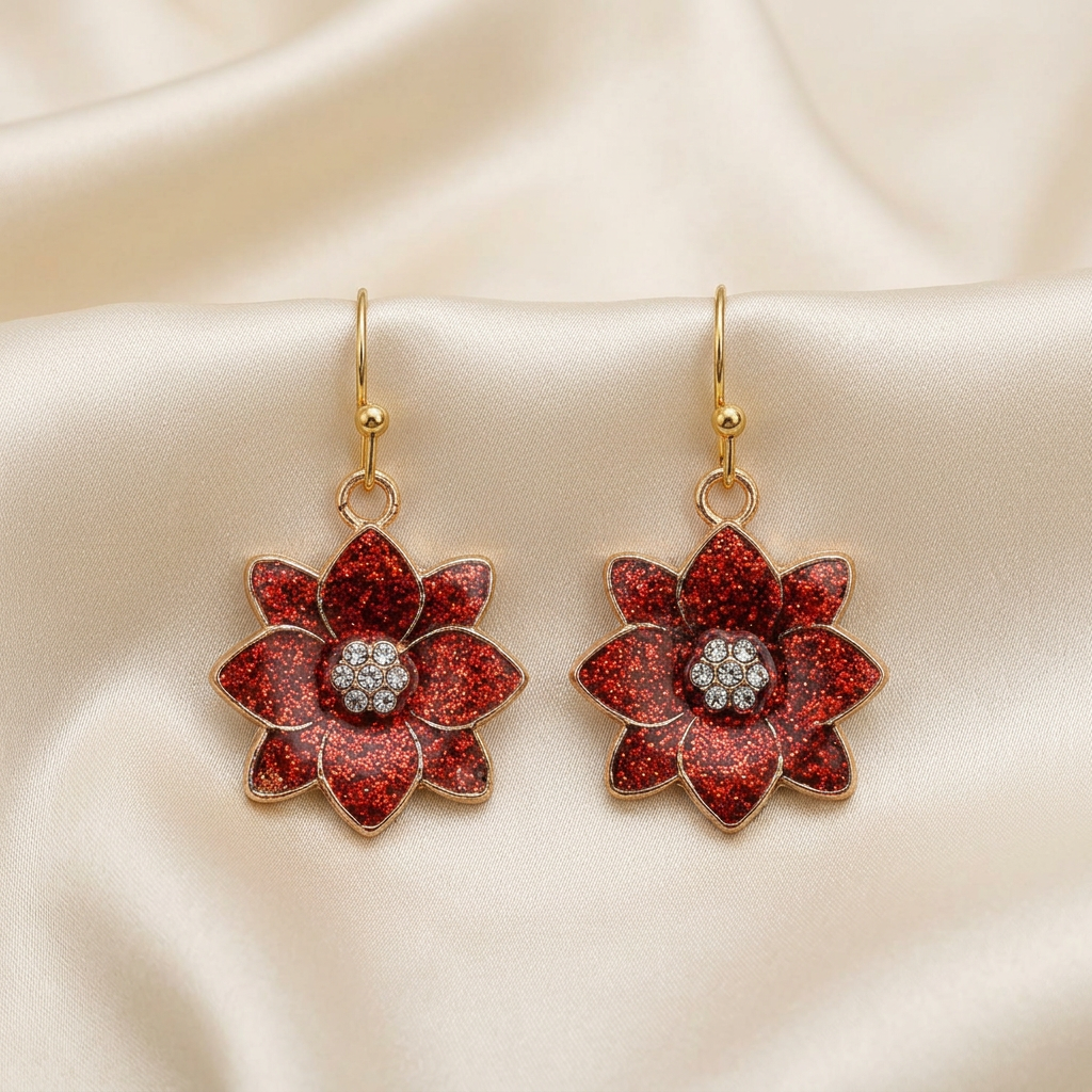 Pair of red glitter flower drop earrings with clear stone centres and gold-tone hooks on ivory satin