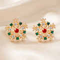 Pair of gold-tone snowflake studs with red centre stones and green and clear accents on ivory satin