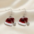 Red Santa hat drop earrings with white bands, rhinestone pom-poms, and silver-tone hooks on ivory satin
